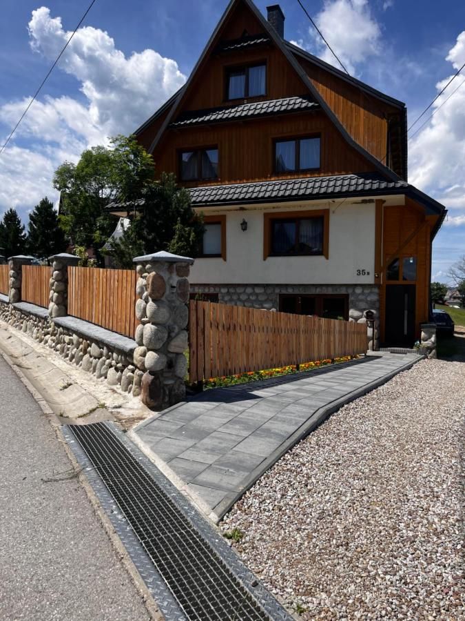 Dom U Stosela z drewnianym piętrem, kamiennym ogrodzeniem i chodnikiem do wejścia